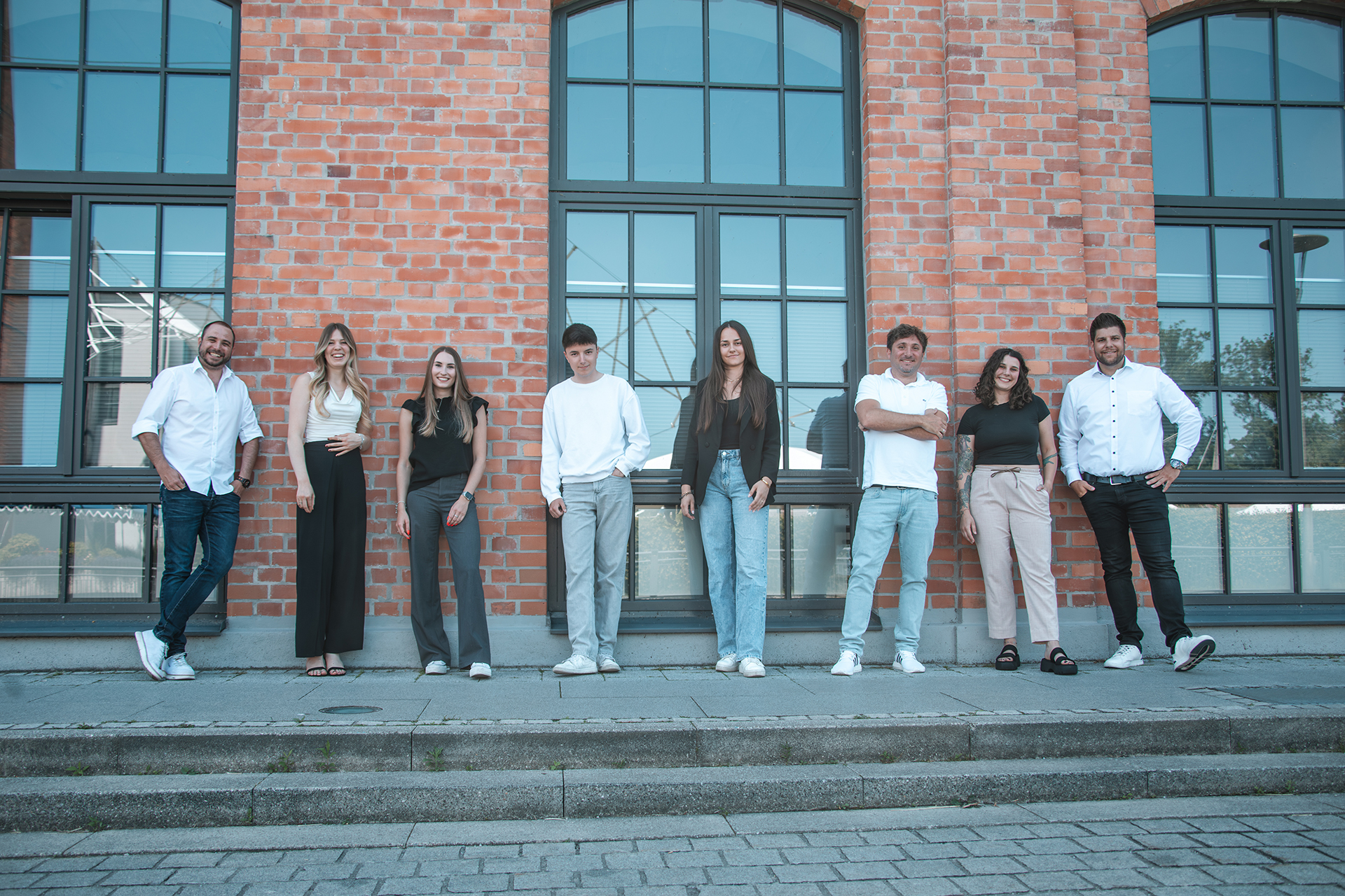 Das Abomate-Team – 8 Teammitglieder vor einem modernen Backsteingebäude